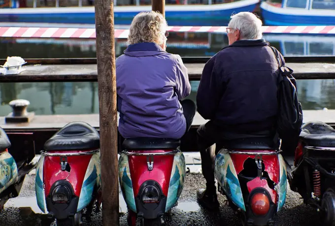 Senior couple sitting on Scooter stools at food stall, Camden market; London, England