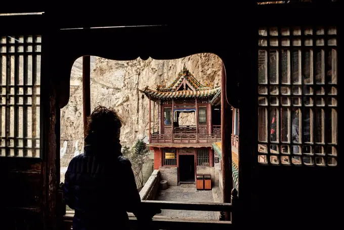 A tourist looking out a window at The Hanging Temple, also known as Hanging Monastery or Xuankong Temple, near Datong; China