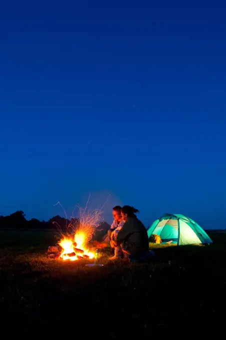 Couple camping with fire outside tent in field