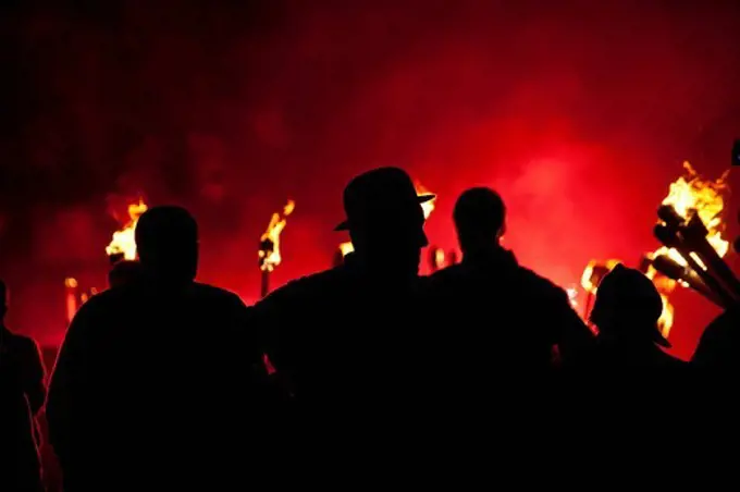 Silhouettes of people in front of red flare and burning torches at Newick Bonfire nightNewick, East Sussex, England. Silhouettes of people in front of red flare and burning torches at Newick Bonfire night