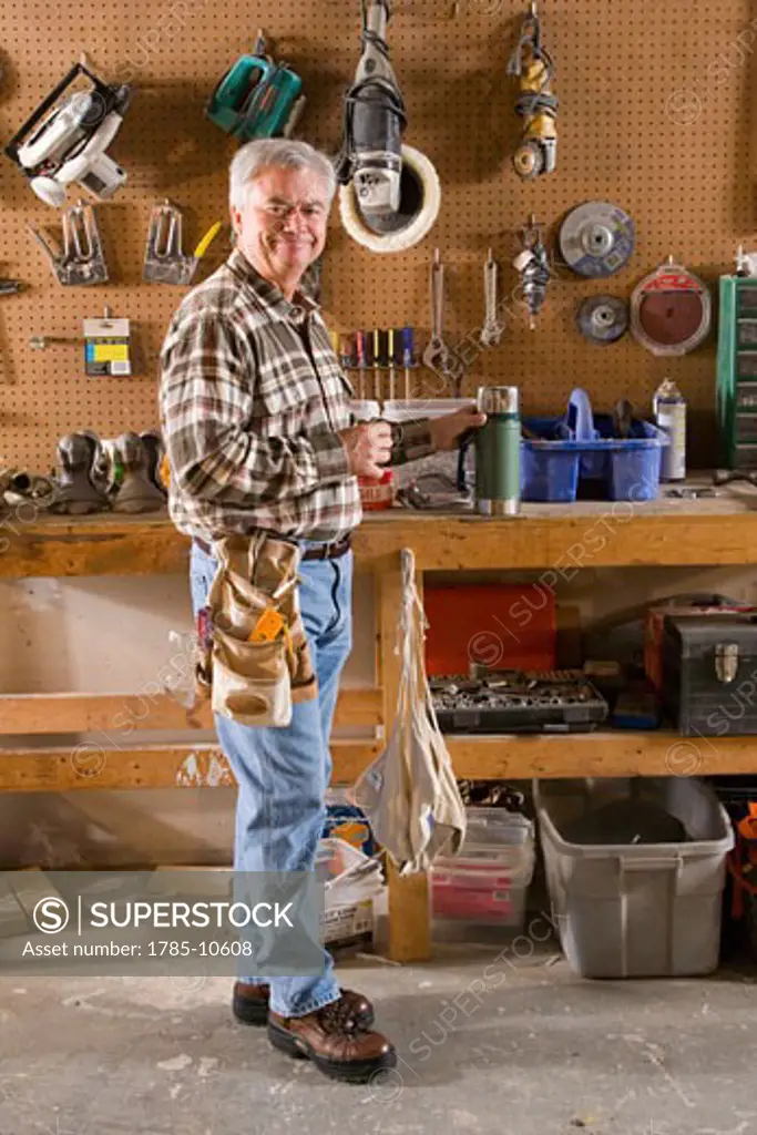 Senior man standing in garage with tools and tool belt