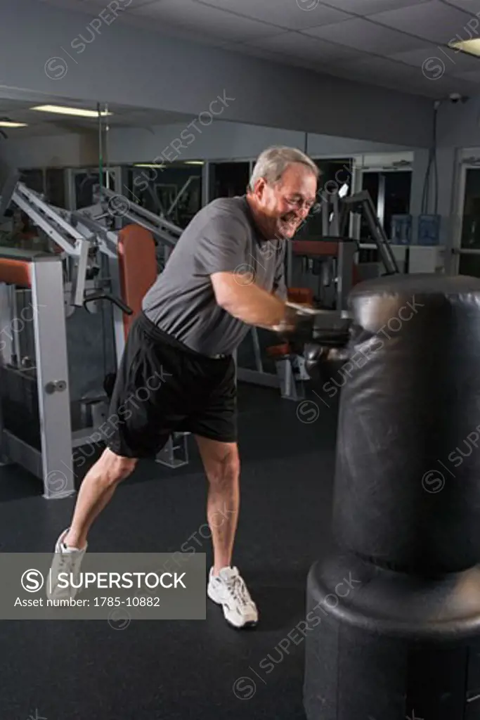 Senior man with boxing gloves hitting punching bag at gym