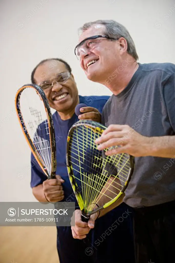 Multi-ethnic senior men laughing and playing racketball at indoor court