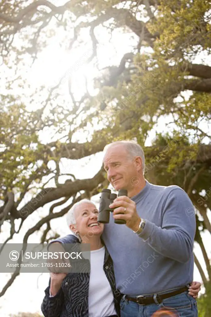 Affectionate senior couple standing together in park watching nature