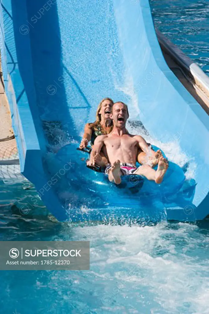 Couple sliding down slide on innertube in water park