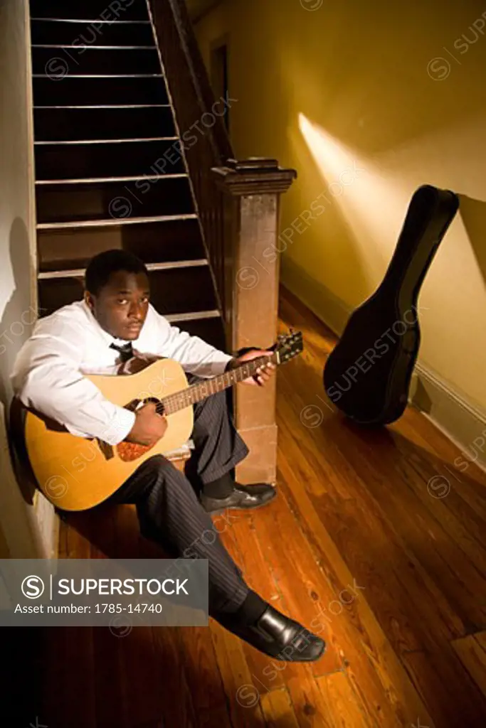 African American musician playing guitar in hallway of house