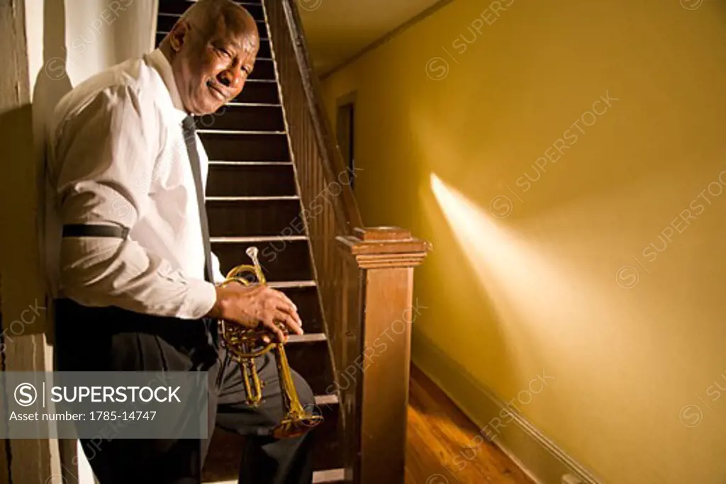 Senior African American jazz musician standing near staircase with trumpet