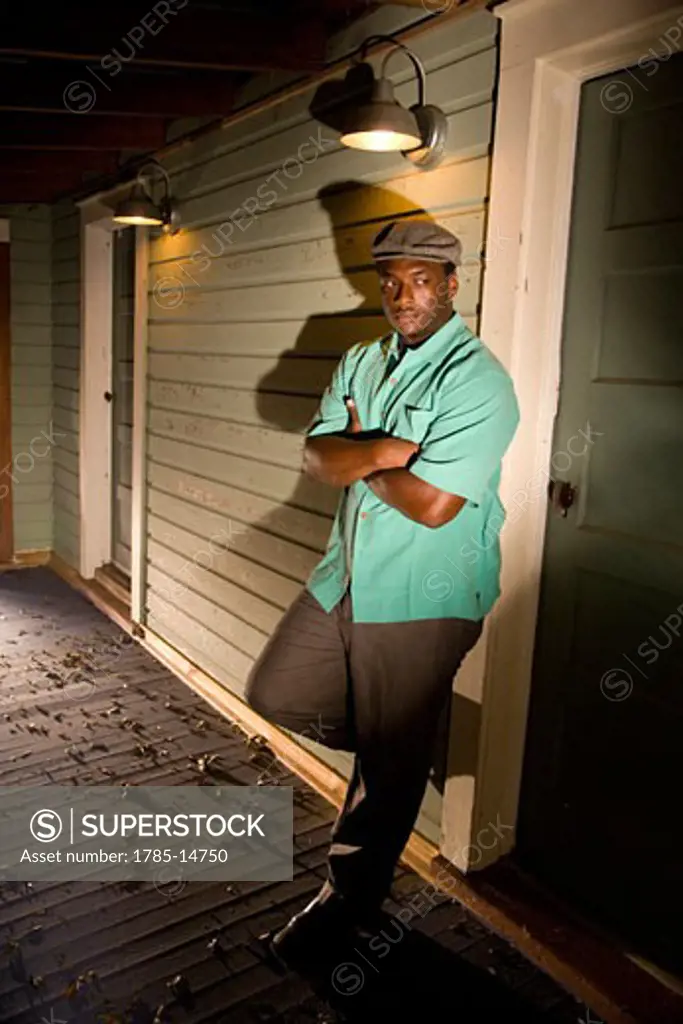 African American man leaning on porch of house at night