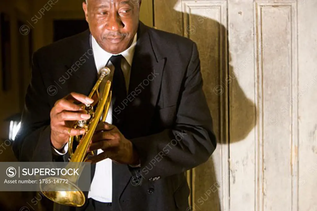 Senior African American musician holding trumpet near door