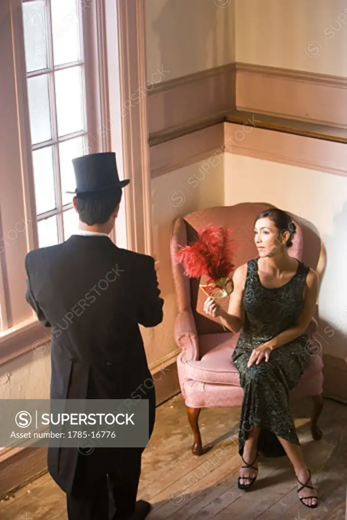 Hispanic woman in formal gown sitting in chair looking at man in tuxedo