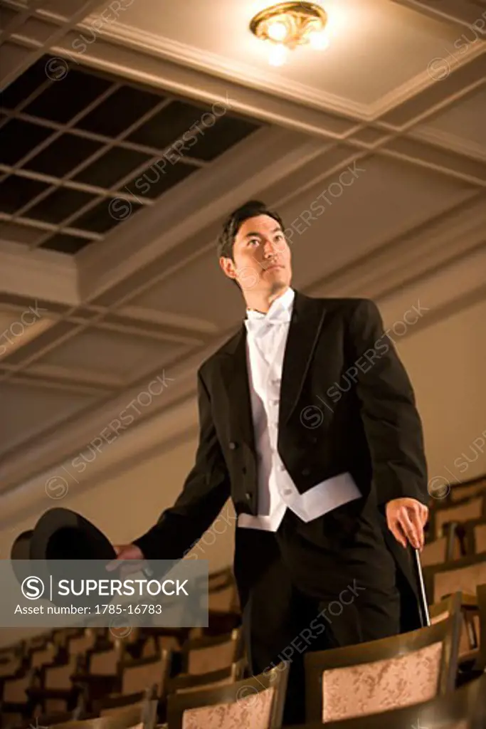 Asian man in tuxedo with top hat and cane standing in empty theater