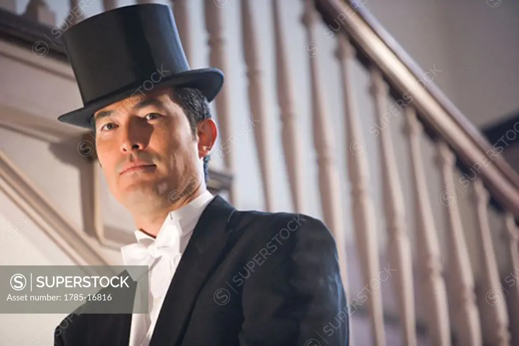 Asian man in tuxedo standing on stairs with top hat
