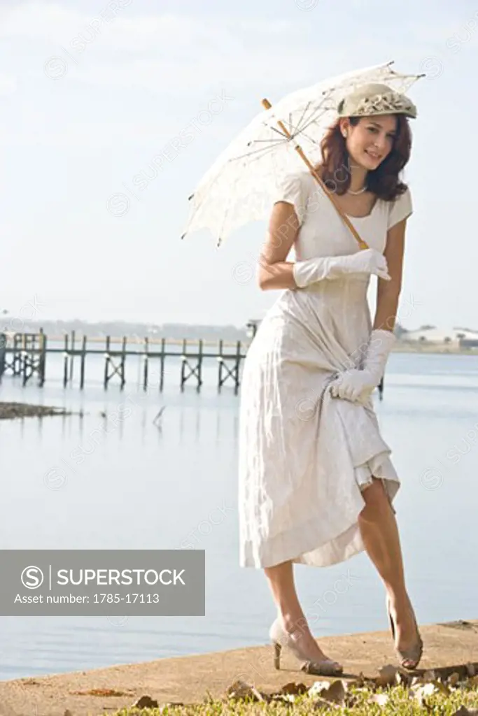 Elegant lady in white dress holding umbrella on water's edge at a garden party