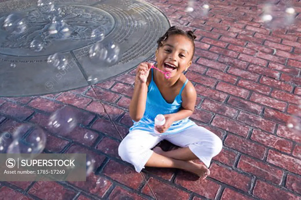 Portrait of African American girl blowing bubbles in park