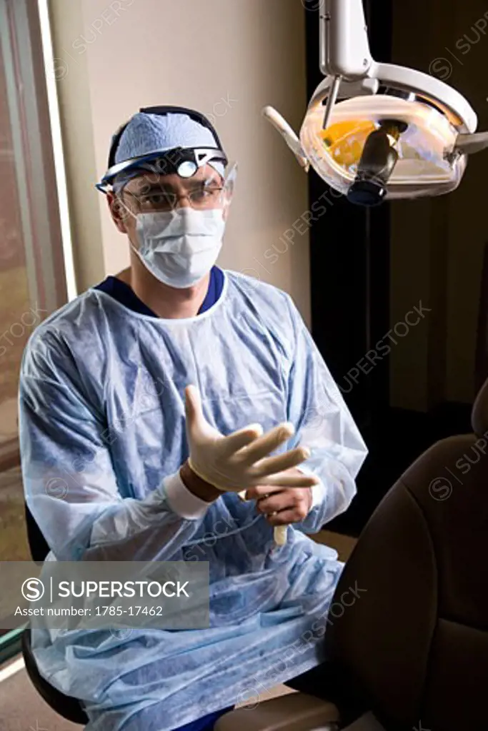 Dentist in scrubs and mask next to exam chair