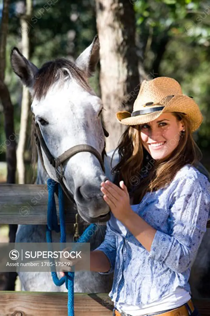 Young cowgirl petting white Gelding horse on farm