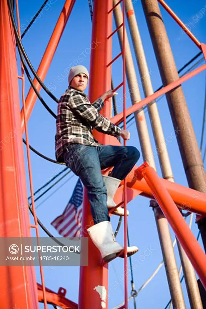 Young fisherman in plaid shirt climbing ladder on fishing boat