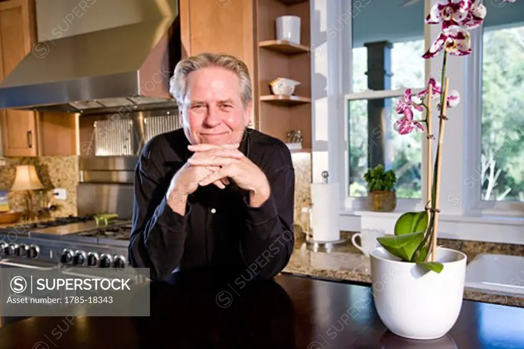 Mature man in kitchen next to orchid flower pot