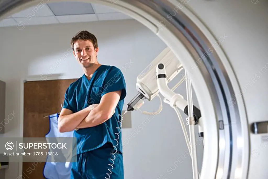 View of healthcare worker in blue scrubs framed by CAT scan machine
