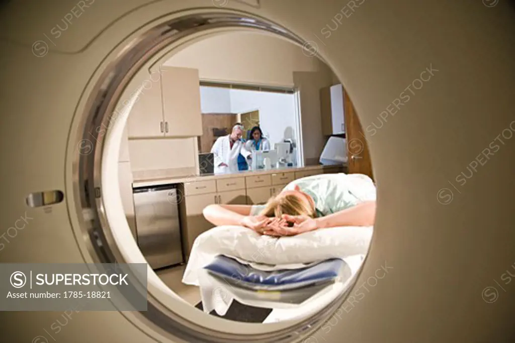 Patient lying on CAT scan machine while doctors consult in background