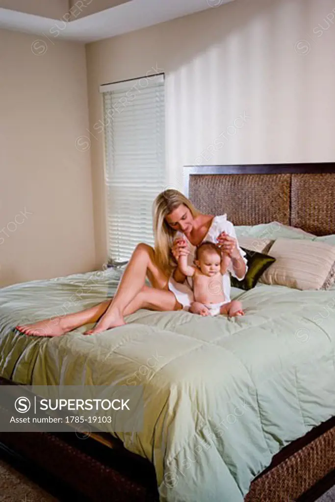 Young mother and 6 month old baby sitting in bedroom