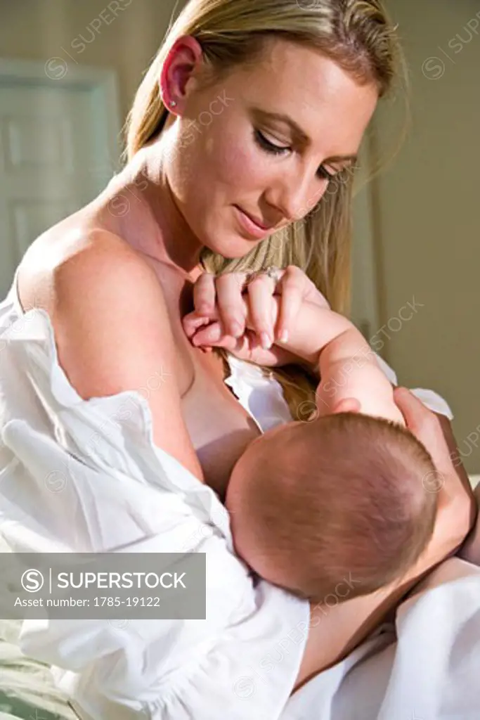 Young mother breastfeeding 6 month old baby in bedroom