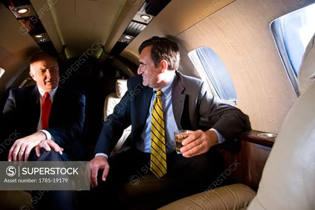 Businessmen with drinks on private jet plane