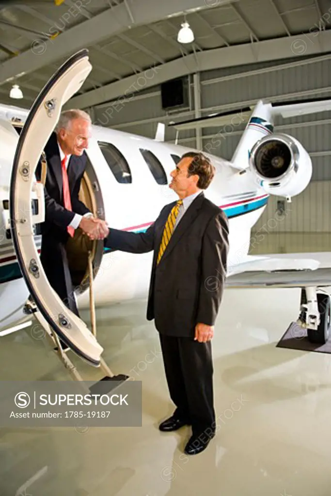 Middle-aged businessmen shaking hands at private jet plane