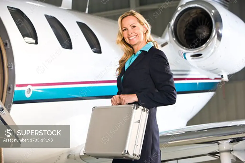 Businesswoman with briefcase standing next to corporate jet