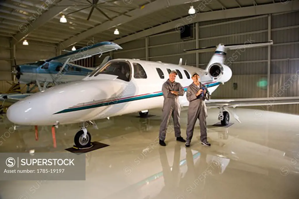 Two airplane mechanics standing next to small planes in hangar