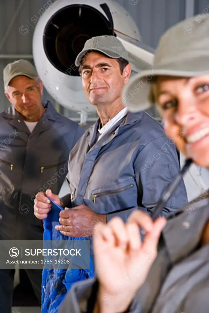 Three airplane mechanics standing next to small planes in hangar