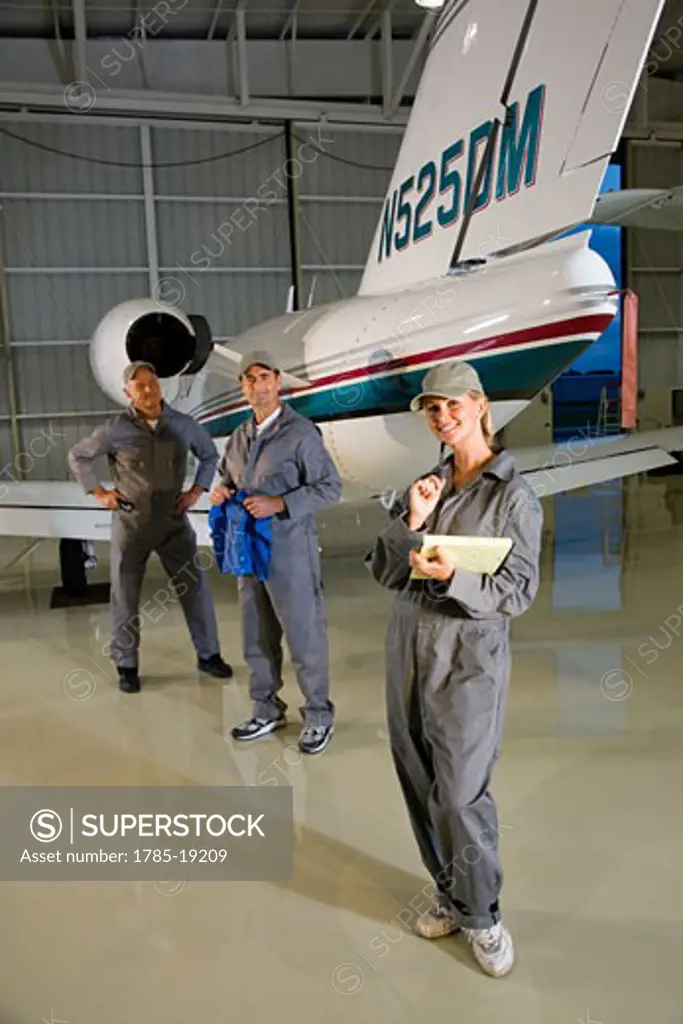 Three airplane mechanics standing next to small planes in hangar