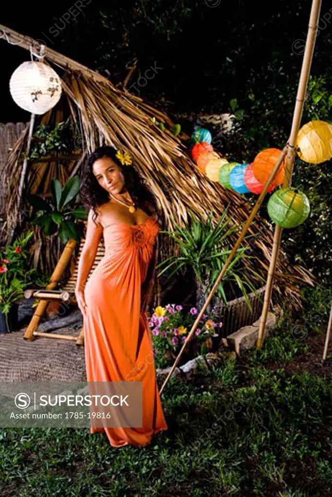 Young Hispanic woman in orange dress standing in tropical garden on island