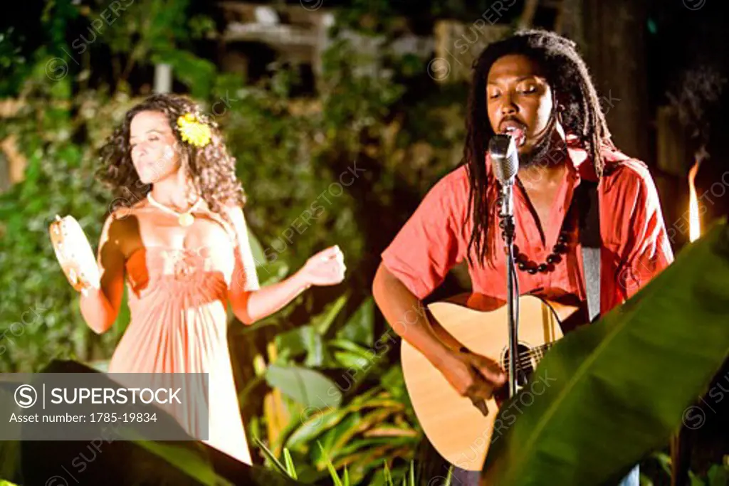 Young Jamaican man singing and playing guitar with Hispanic woman on tambourine