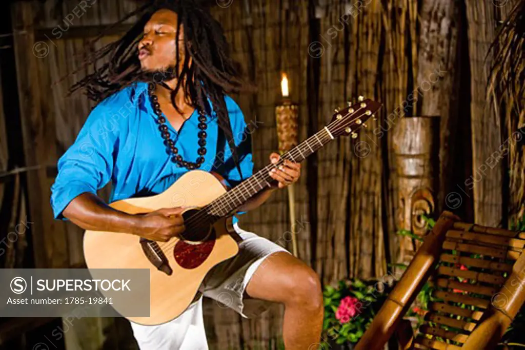 Young Jamaican man with dreadlocks playing guitar on tropical island