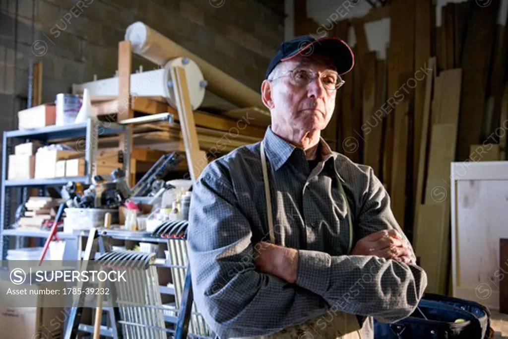 Senior man in woodworking shop by storage shelves