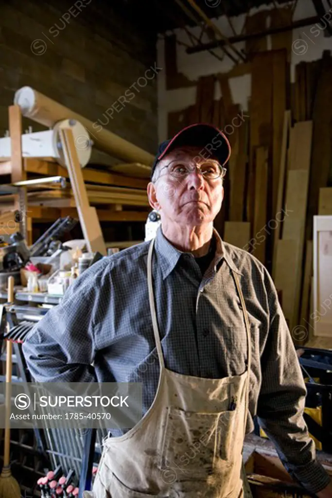 Senior man in woodworking shop by storage shelves