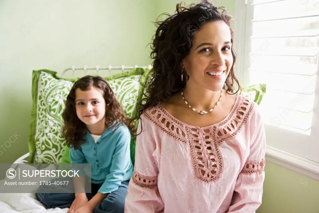 Hispanic mother and pretty little girl sitting together on bed