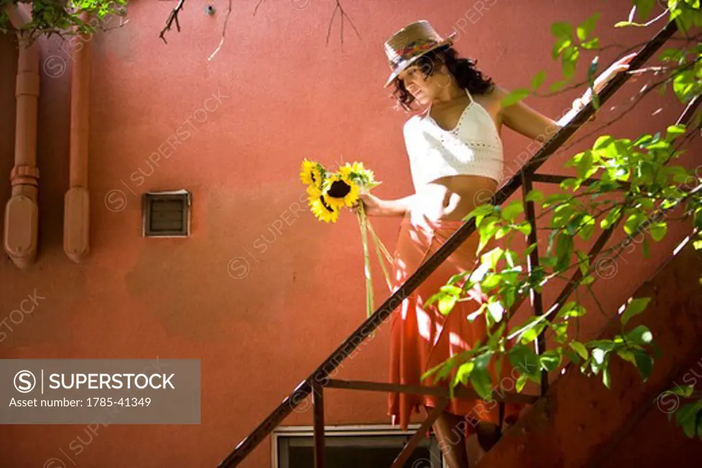 Wistful young Hispanic woman on staircase holding sunflowers