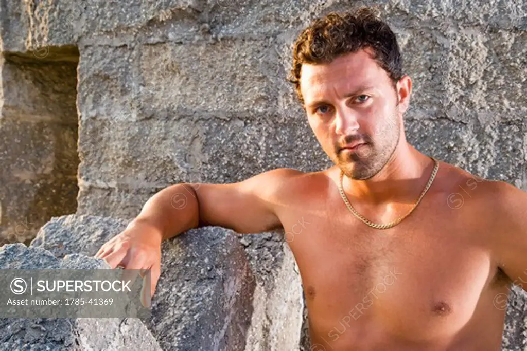 Serious young man with no shirt standing against stone wall