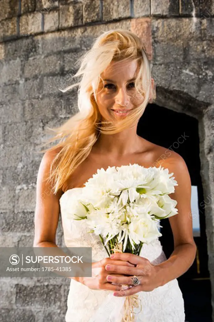 Smiling young bride holding bouquet outdoors