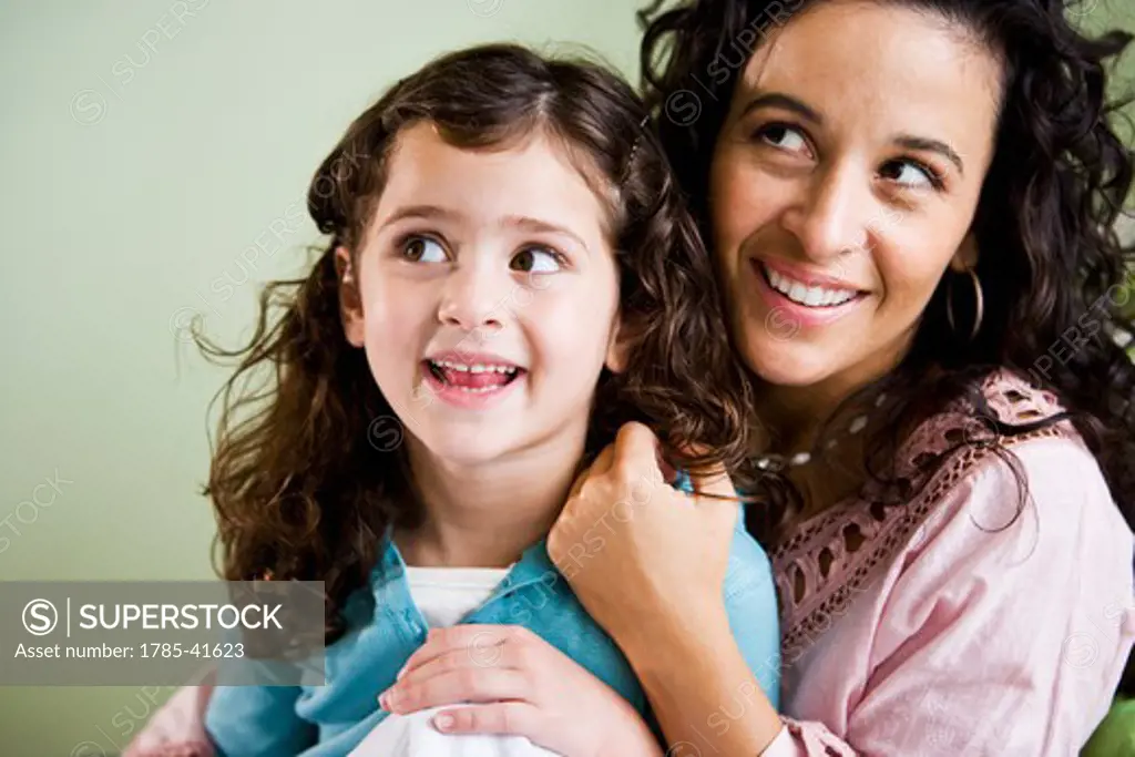 Headshot of Hispanic mother and young daughter smiling and looking up