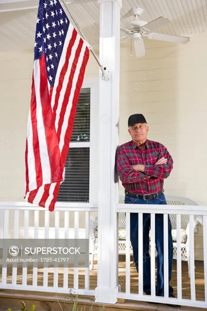 Senior man standing by American flag on porch
