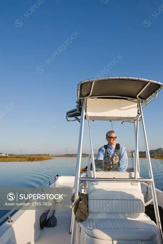 Happy middle-aged man driving fishing boat on river