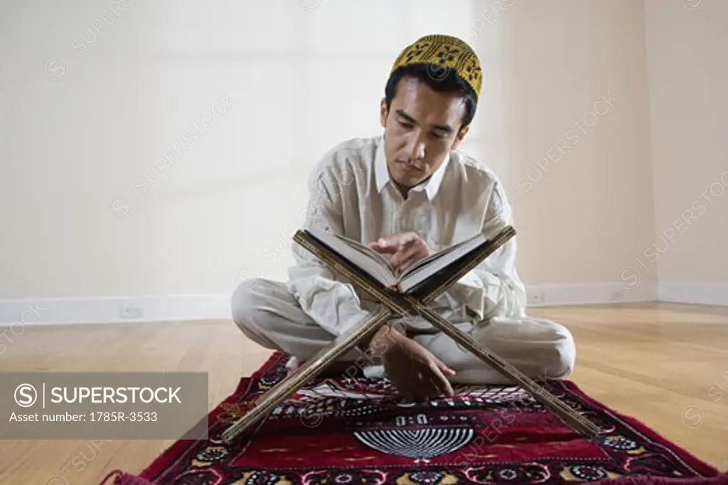 A Muslim man reading Koran on a prayer mat