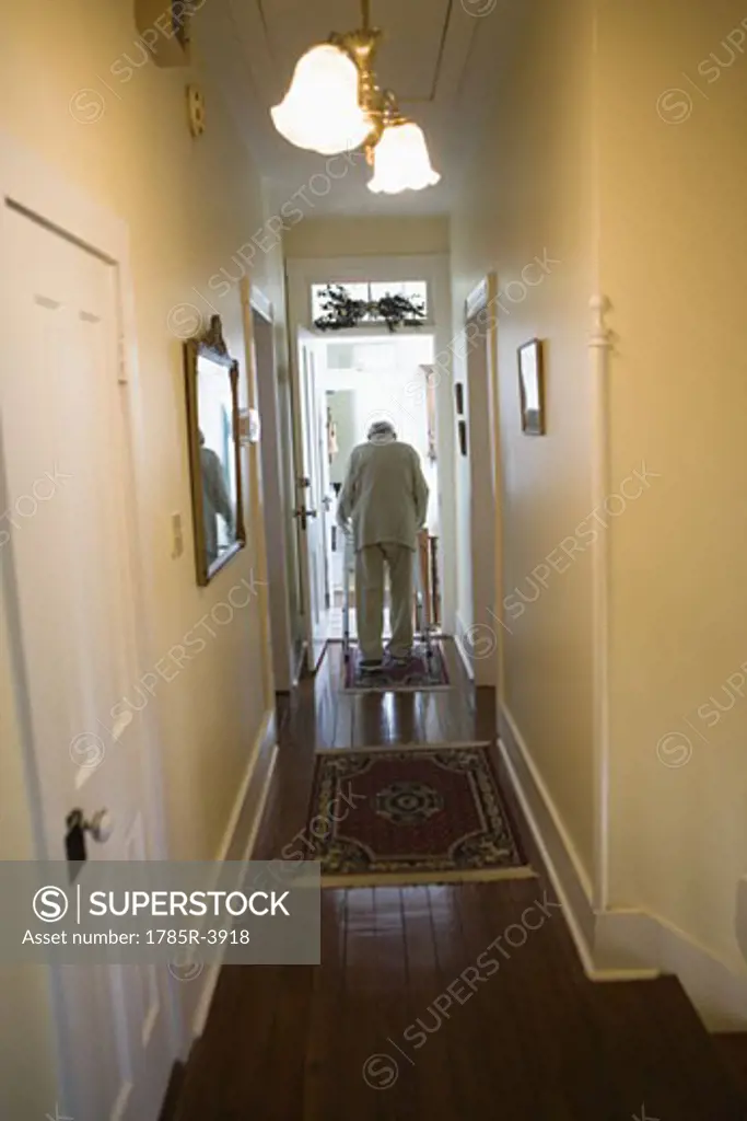 Feeble senior man slowly going down hallway with walker