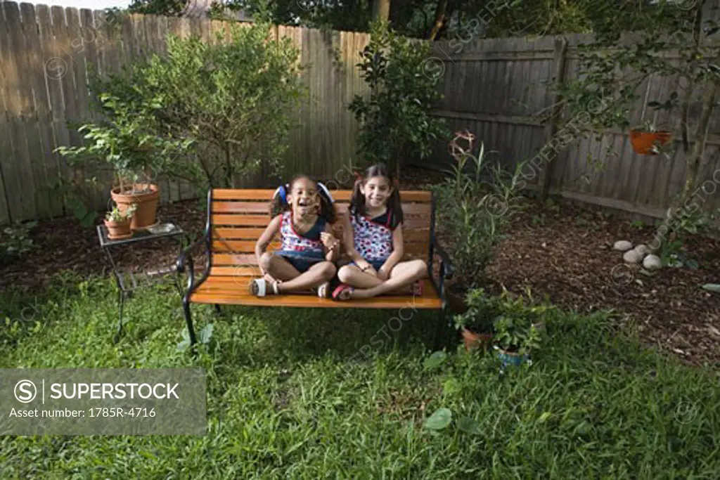 Portrait of cheerful girls (6-7) sitting on a bench in a backyard
