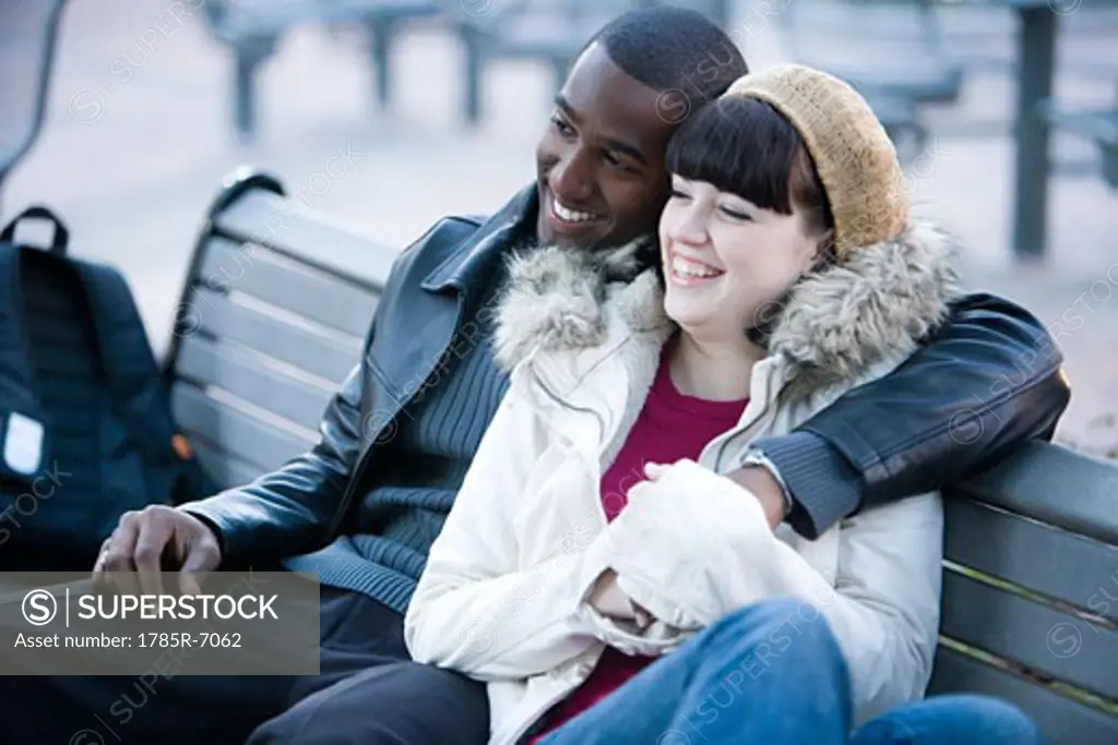 Cheerful young inter-racial couple embracing on a park bench