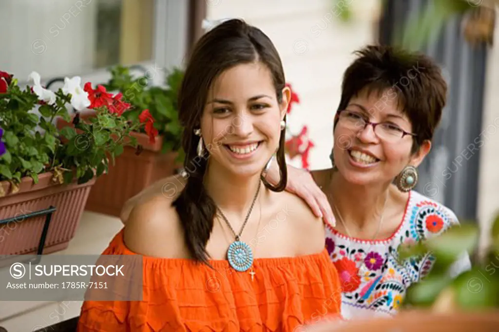Mexican mother and daughter sitting together on front porch of house