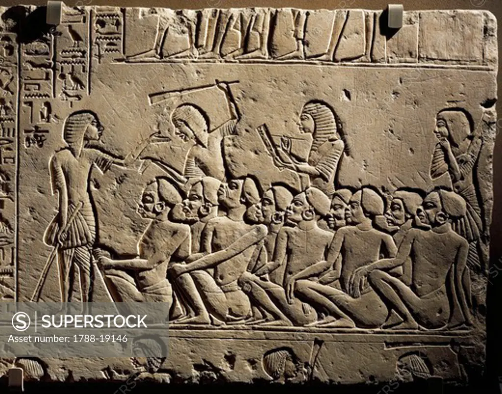 A group of Negroid prisoners surrounded by guards armed with clubs while a scribe draws up a report, relief from the tomb of Horemheb at Saqqara